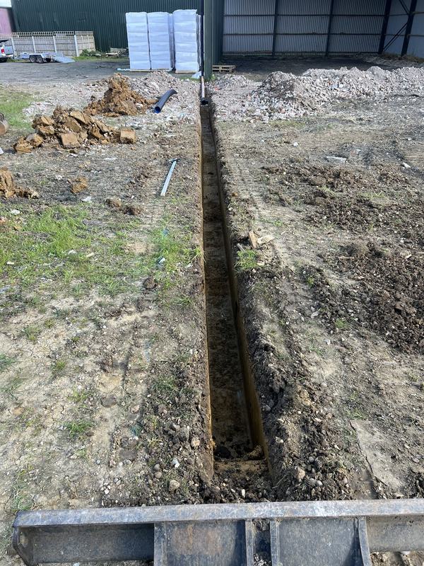 Long drainage trench dug alongside agricultural barns, seen from the mini digger