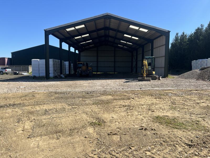 Large open-sided agricultural barn with the reinstated yard in front and a mini digger parked
