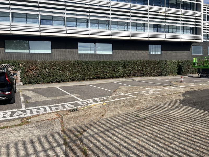 Neatly cut, straight-topped hedge running along a commercial car park in front of an office building