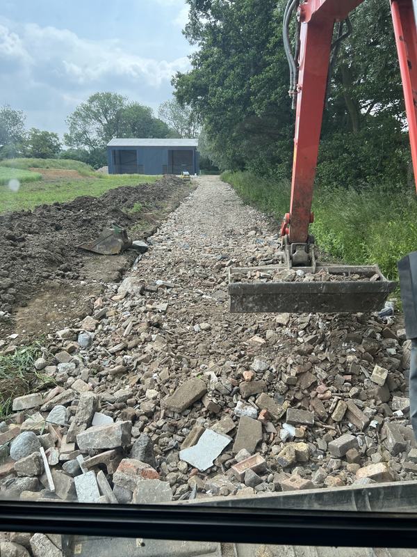 Completed track filled with crushed hardcore leading towards a barn, seen from the digger cab