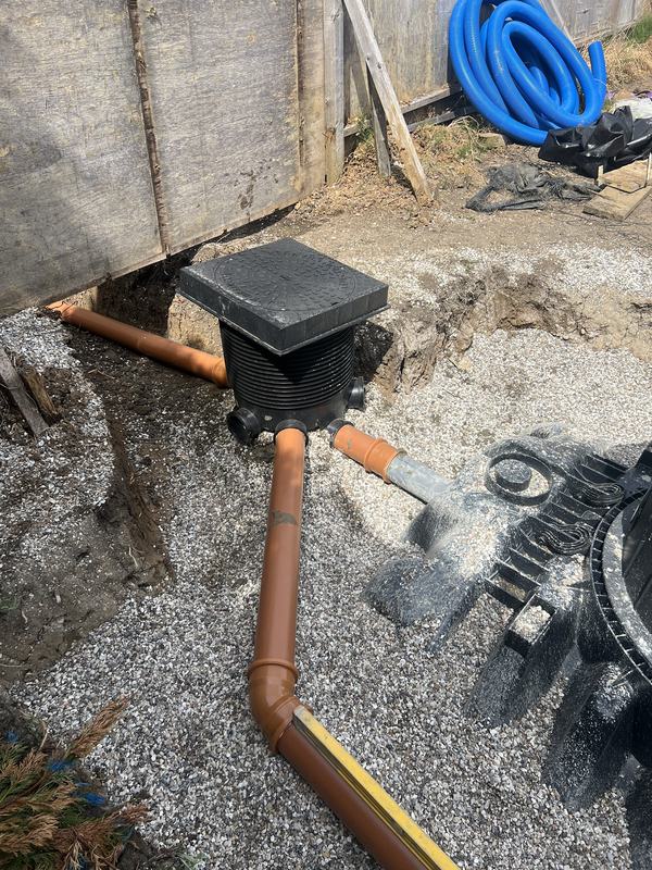 Inspection chamber with cover connected to orange drainage pipework in a gravel bed