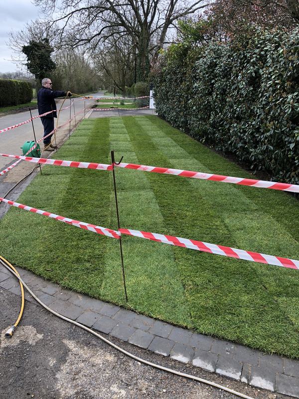 Freshly laid striped turf along a roadside frontage being watered in, taped off to keep people off while it roots