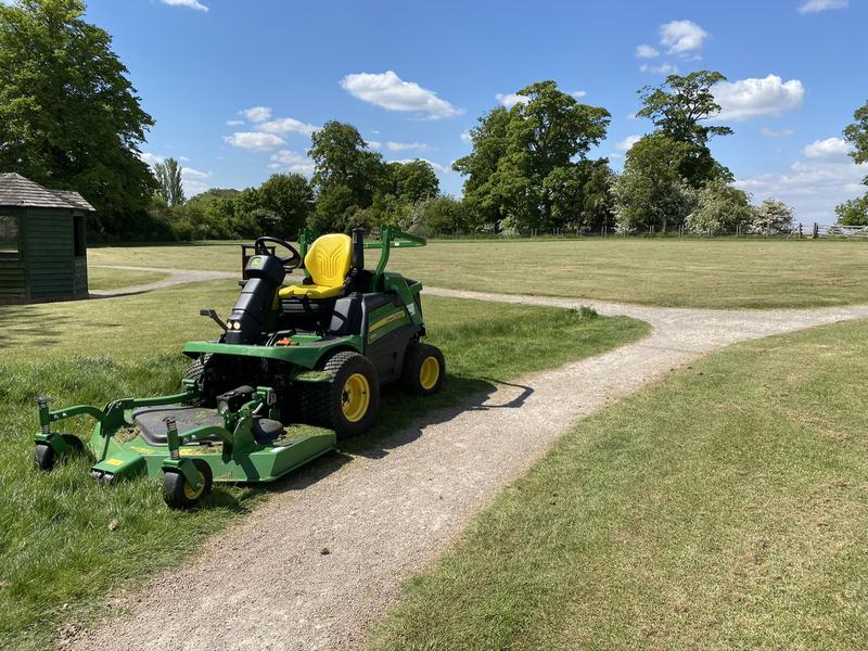 Green John Deere out-front ride-on mower parked beside a gravel path in parkland