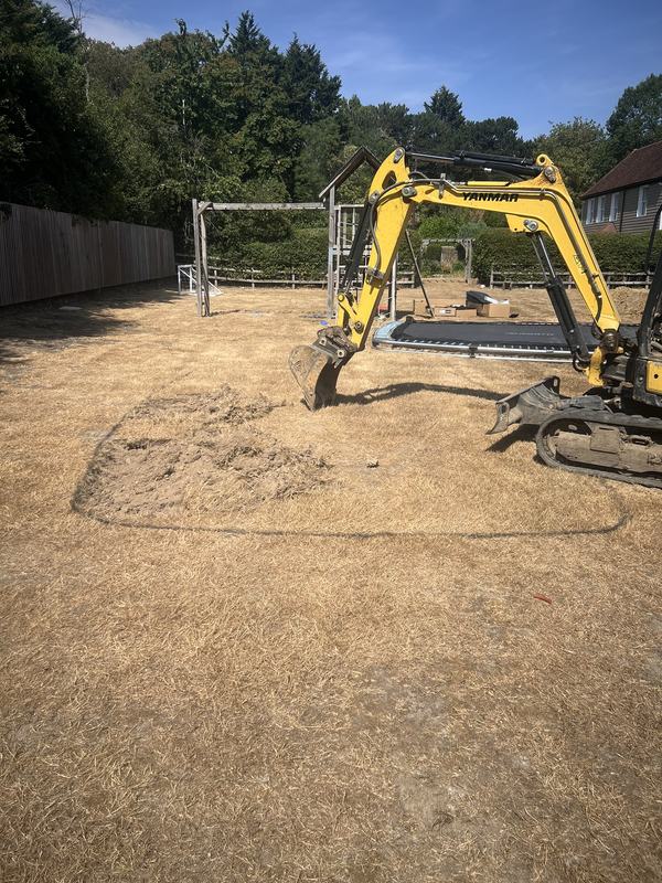Yellow Yanmar mini digger starting to excavate a marked-out area on a lawn for an in-ground trampoline