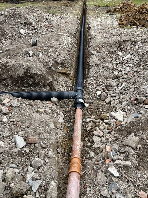Black twin-wall drainage pipe with a tee junction and orange pipe laid in a trench
